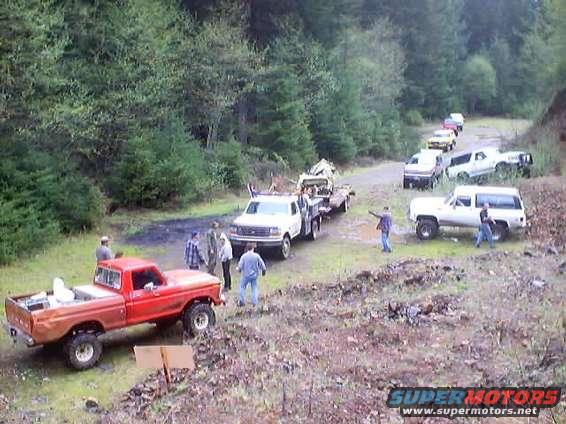Several trucks and SUVs parked on a dirt road with trees in the background