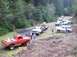 1976 Ford F-100 - A group of trucks and SUVs are gathered on a dirt road in a wooded area.