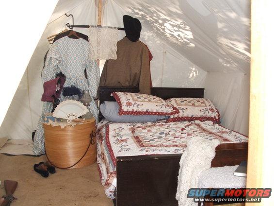 Interior of a tent with a bed, period clothing, and a fan