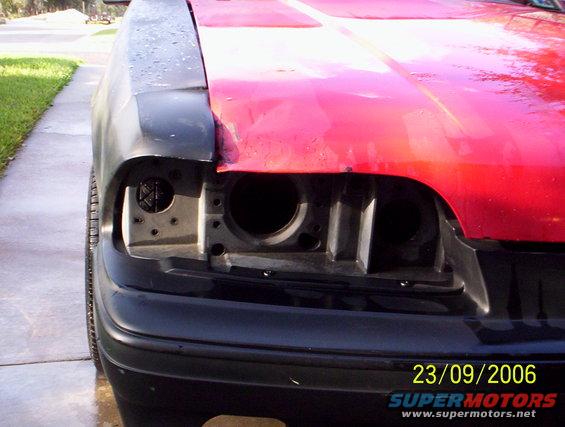 Car front end with missing headlights, red hood, and black bumper