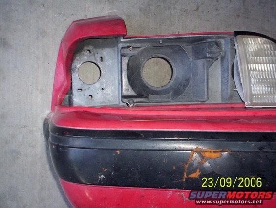 Red car bumper with black trim and a damaged headlight assembly, showing rust spots