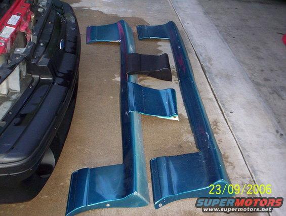 Teal side skirts and front bumper section laid out on concrete
