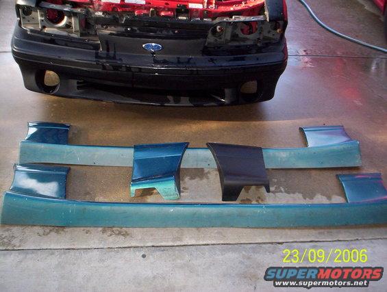 Ford Mustang body kit parts laid out on concrete, with the front of a car visible in the background