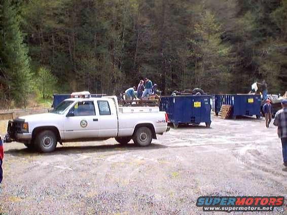 White pickup truck with people loading items into the bed, next to blue dumpsters