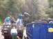 1976 Ford F-100 - People are disposing of old tires by loading them into a large blue dumpster.