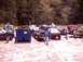 1976 Ford F-100 - A scene of multiple trucks and people in a salvage yard, with large blue dumpsters present.