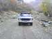 1978 Ford Bronco - A blue 1978 Ford Bronco is seen from the front on a dirt road, surrounded by autumnal foliage and rocky terrain.