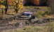 1979 Ford Bronco - A pink SUV is deeply mired in mud on an off-road trail during autumn.