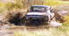 1979 Ford Bronco - Ford Bronco navigating a muddy trail, splashing water and dirt.