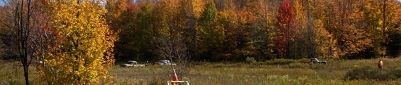 two trucks parked in a grassy field with fall foliage in the background