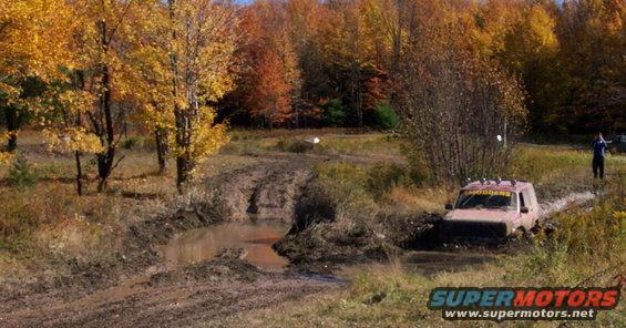 Red SUV stuck in mud pit with fall foliage in background