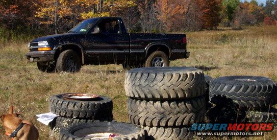 Black pickup truck parked in a grassy field with stacks of tires in the foreground