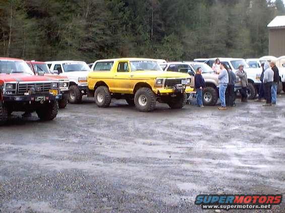 Yellow Ford Bronco parked with other trucks. Some people are standing around