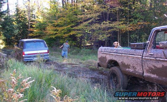 Rear view of a 1979 Ford Bronco stuck in mud, being pulled by a pickup truck