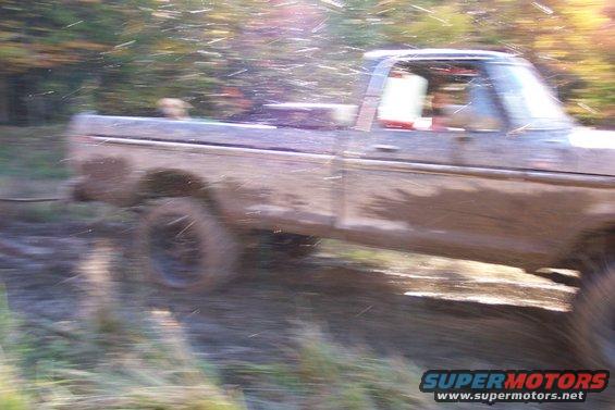 Muddy 1979 Ford F-Series pickup truck driving through off-road terrain with water splashing