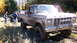 1979 Ford Bronco - A muddy pickup truck is stuck in the woods with two people observing the situation.