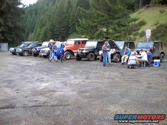 Several off-road vehicles parked in a lot with people gathered around one of them
