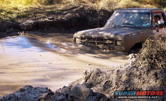 Muddy truck stuck in mud pit, front grille and headlights visible