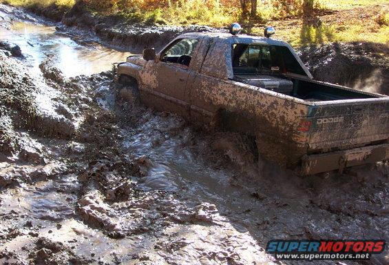 Muddy Dodge pickup truck struggling through a deep mud pit on a trail