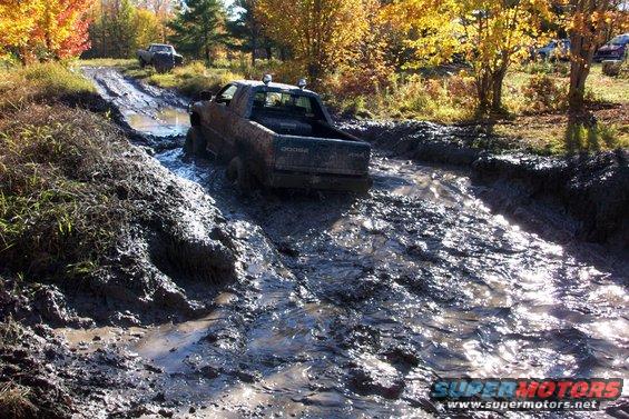 Muddy Dodge pickup truck with two lights on the roof driving through a muddy track