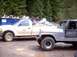 1976 Ford F-100 - A silver Jeep CJ-7 is parked next to a white pickup truck, with a blue dumpster in the background.