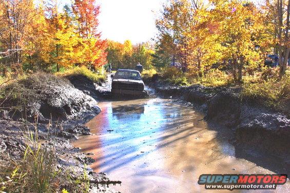Truck driving through mud puddle with fall foliage