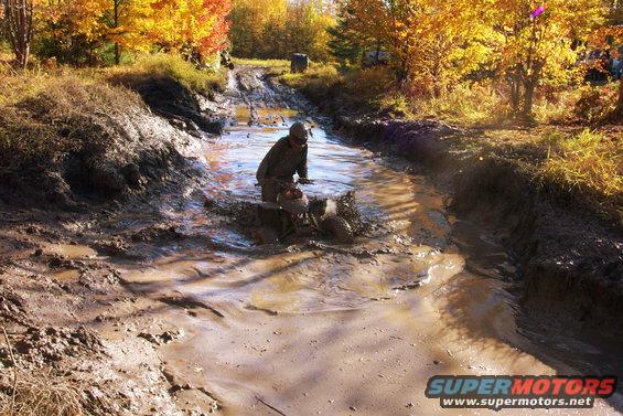 ATV splashing through a muddy ditch with autumn trees in the background