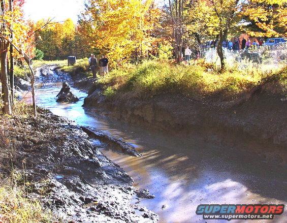 Off-road vehicle navigating a muddy track with spectators in the background