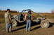 1979 Ford Bronco - A heavily modified off-road vehicle sits in a field with two people nearby under a clear blue sky.