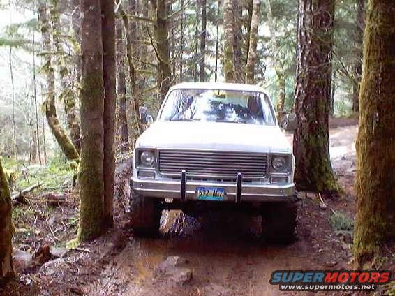 White pickup truck driving through a muddy forest path