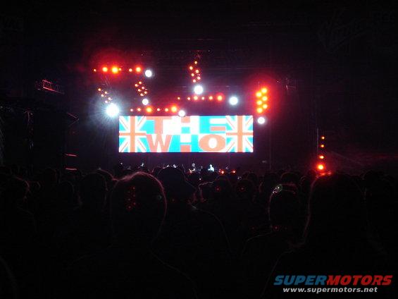 Concert stage with "THE WHO" logo displayed on a large screen, audience in foreground