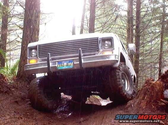 White pickup truck with a large grille and chrome bumper, off-roading on a muddy trail