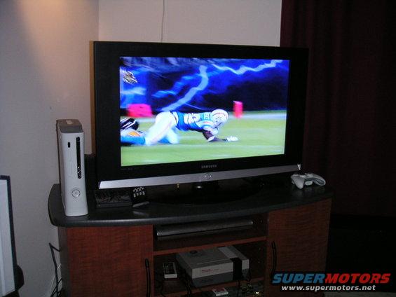 TV displaying a football player on the field, with an Xbox 360 and game consoles nearby