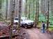 1976 Ford F-100 - A white Ford F-150 truck navigates a wooded trail with a person standing nearby.
