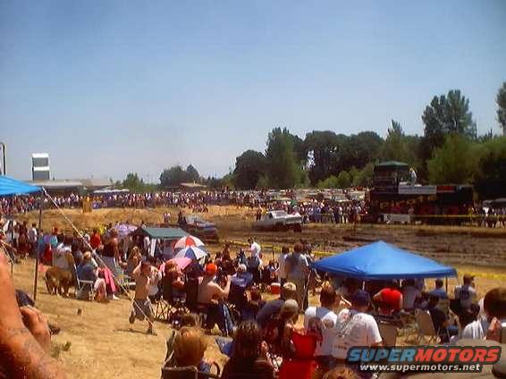 Crowd gathered at a mud run event with tents and vehicles in the background