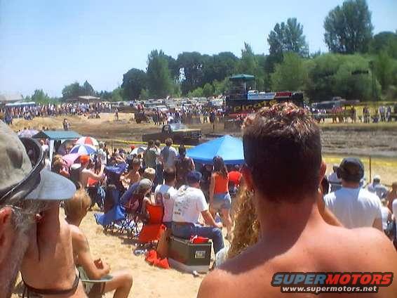 Crowd watching a mud bog event with several trucks in the background
