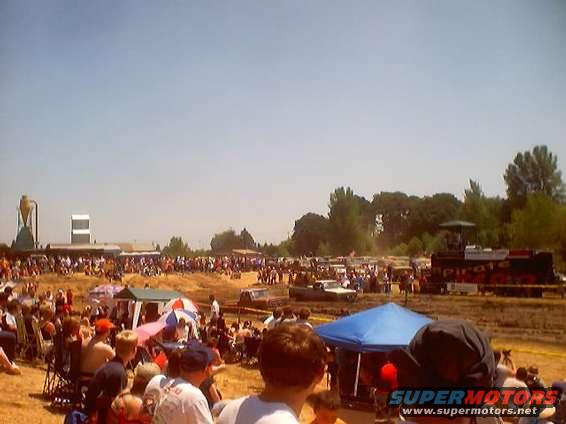 Spectators watch a mud bogging event with trucks and tents set up