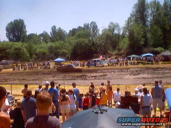 Mud bogging event with spectators and vehicles in the background