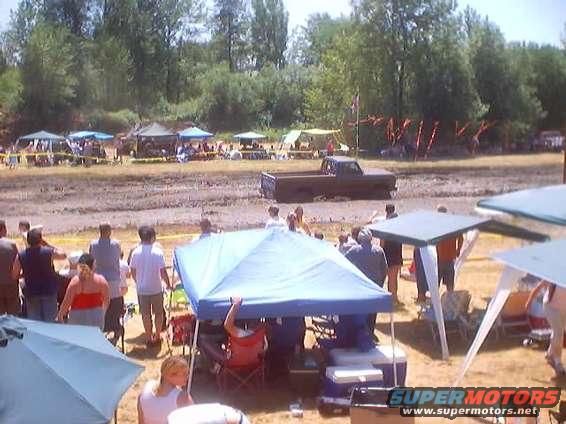 Muddy field with tents set up and a dark-colored pickup truck stuck in the mud