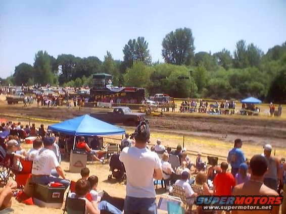 Mud bog event with spectators and trucks in the background