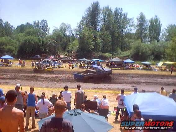 Mud bog event with several trucks and spectators gathered around a muddy track
