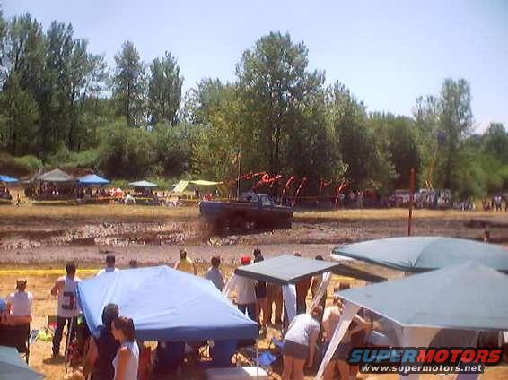 Truck in mud pit with people watching from under tents