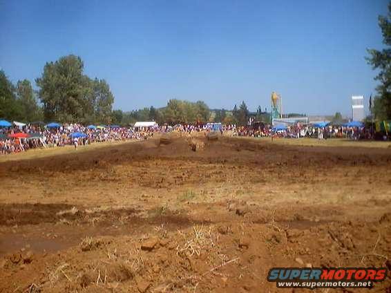 Muddy motocross track with crowds watching under tents and blue sky