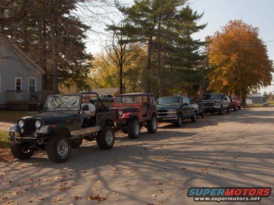 1979 Jeep CJ5 in front of a line of other vehicles parked on a street with fall foliage