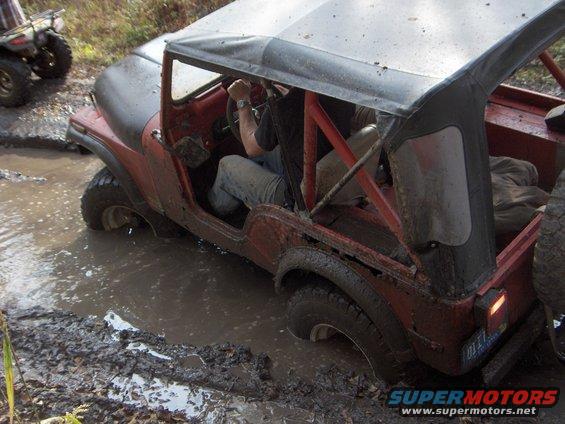 Red Jeep CJ stuck in mud, with an ATV in the background