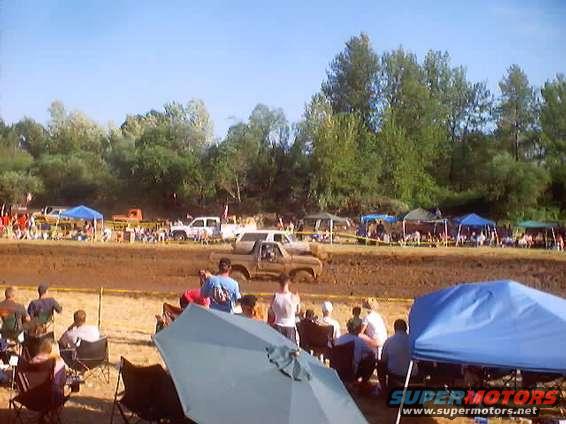 Truck stuck in mud pit at an event, spectators watching from the side