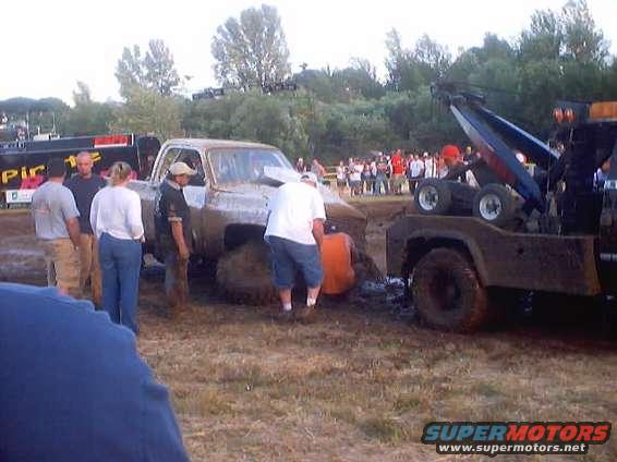 Mud-covered 1973 Ford F-150 pickup truck stuck in mud, being pulled by a tow truck