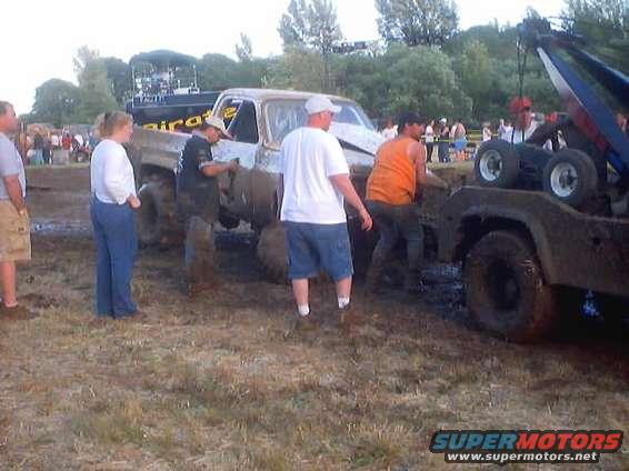 1976 Ford F-100 pickup truck stuck in mud, being towed by a tow truck