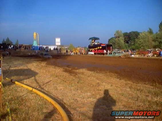 Muddy field with a yellow hose in the foreground and a crowd gathered around a stage with 'PIRATE RADIO' text