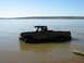 1990 Ford Bronco - A pickup truck navigates through a body of water under a clear blue sky.